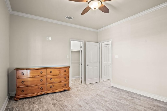 unfurnished bedroom featuring a walk in closet, light wood-type flooring, ceiling fan, and crown molding