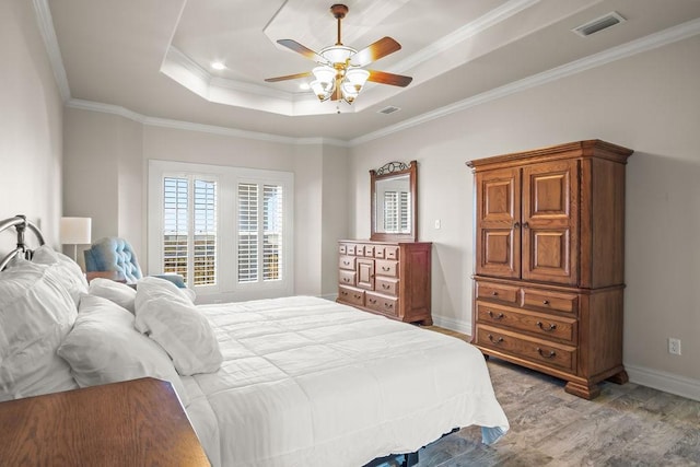 bedroom with light hardwood / wood-style flooring, a raised ceiling, ceiling fan, and ornamental molding