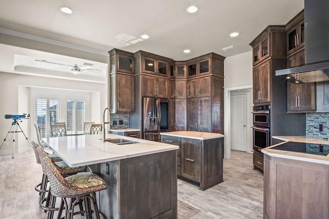 kitchen with sink, stainless steel appliances, light hardwood / wood-style floors, decorative backsplash, and a center island with sink