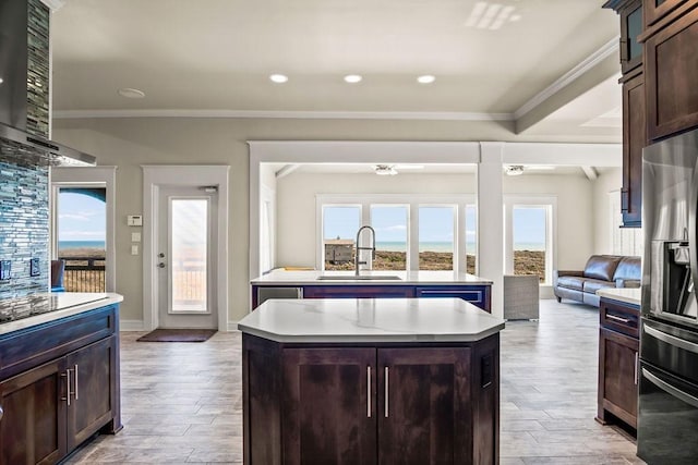 kitchen featuring sink, wall chimney exhaust hood, stainless steel fridge with ice dispenser, a kitchen island, and ornamental molding