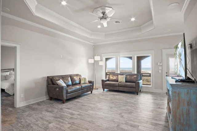 living room featuring hardwood / wood-style floors, a tray ceiling, ceiling fan, and ornamental molding