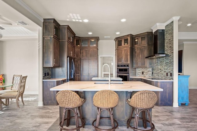 kitchen with decorative backsplash, sink, a kitchen island with sink, and wall chimney range hood