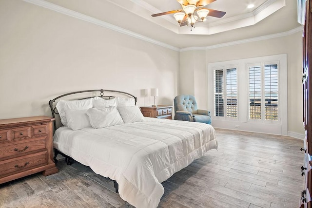 bedroom featuring hardwood / wood-style flooring, ceiling fan, ornamental molding, and a tray ceiling