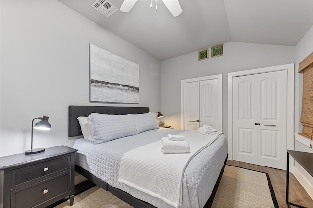 bedroom featuring lofted ceiling, hardwood / wood-style floors, two closets, and ceiling fan