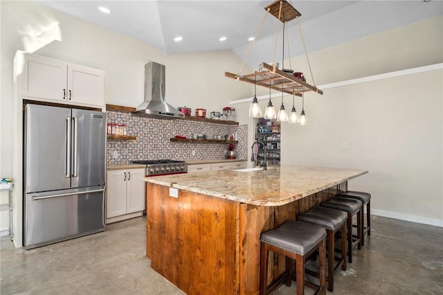 kitchen featuring appliances with stainless steel finishes, wall chimney exhaust hood, vaulted ceiling, a center island with sink, and white cabinetry