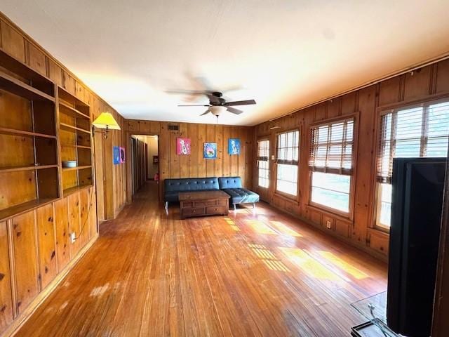 unfurnished living room featuring ceiling fan, wooden walls, and hardwood / wood-style floors