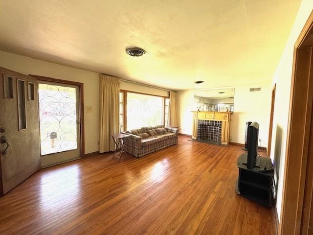 unfurnished living room with a tiled fireplace, visible vents, and wood finished floors