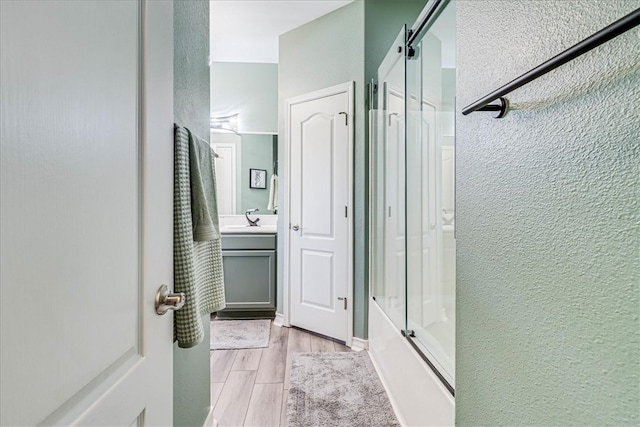 bathroom with bath / shower combo with glass door, wood-type flooring, and vanity