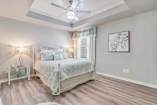 bedroom with hardwood / wood-style floors, ceiling fan, crown molding, and a tray ceiling