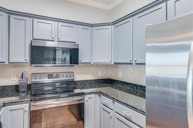 kitchen with crown molding, dark stone counters, appliances with stainless steel finishes, gray cabinets, and decorative backsplash