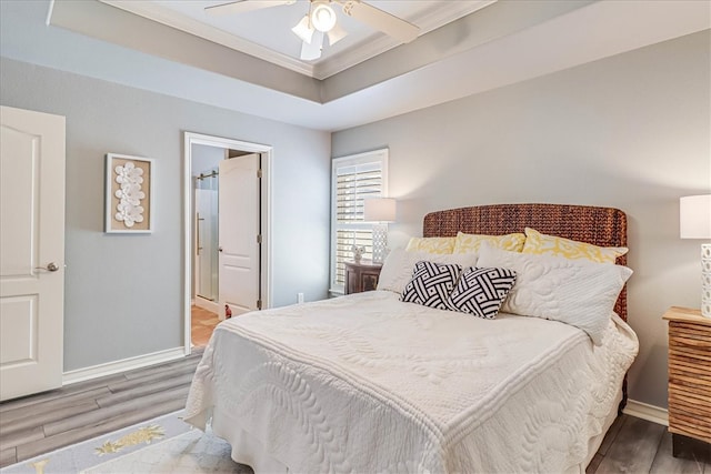 bedroom featuring hardwood / wood-style floors, ensuite bathroom, ceiling fan, and a tray ceiling