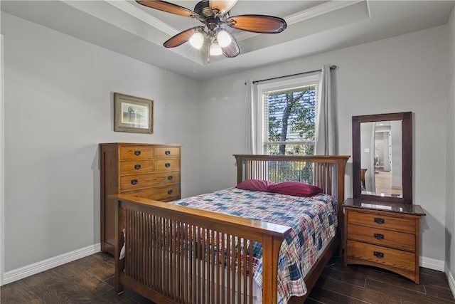 bedroom featuring dark hardwood / wood-style flooring, ceiling fan, crown molding, and a tray ceiling