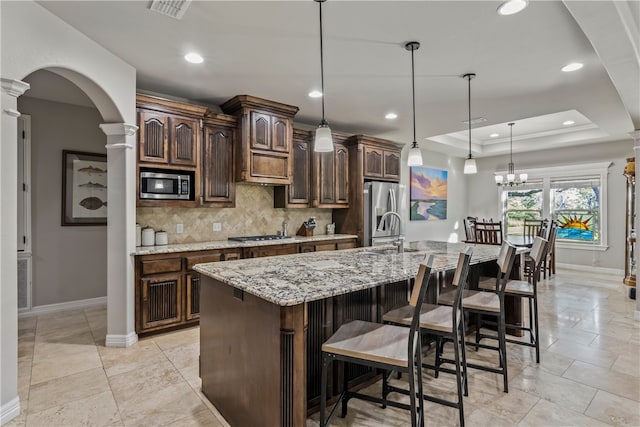 kitchen with stainless steel appliances, dark brown cabinetry, a large island, decorative columns, and pendant lighting