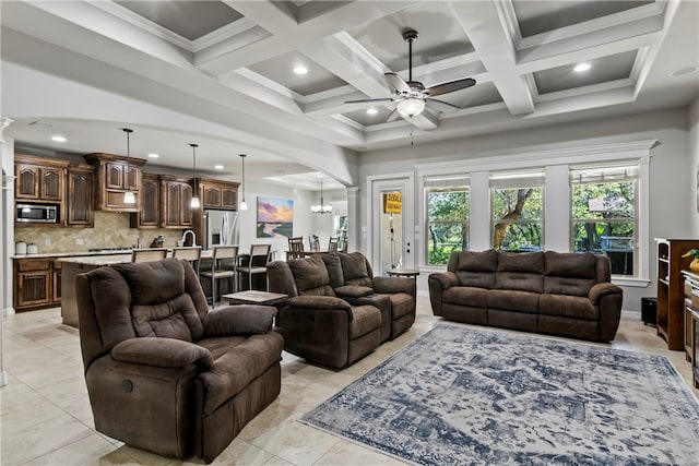 tiled living room featuring beamed ceiling, coffered ceiling, ornamental molding, and ceiling fan with notable chandelier