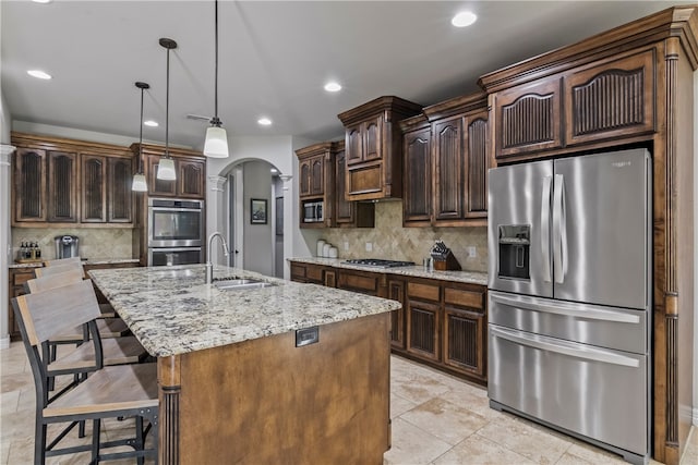 kitchen with appliances with stainless steel finishes, dark brown cabinets, pendant lighting, sink, and a kitchen island with sink