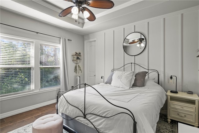 bedroom with ceiling fan, dark hardwood / wood-style floors, a raised ceiling, and crown molding