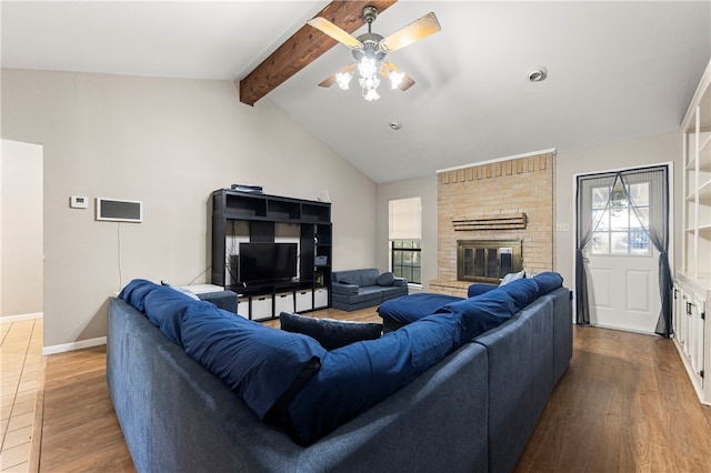 living room with ceiling fan, hardwood / wood-style floors, lofted ceiling with beams, and a brick fireplace