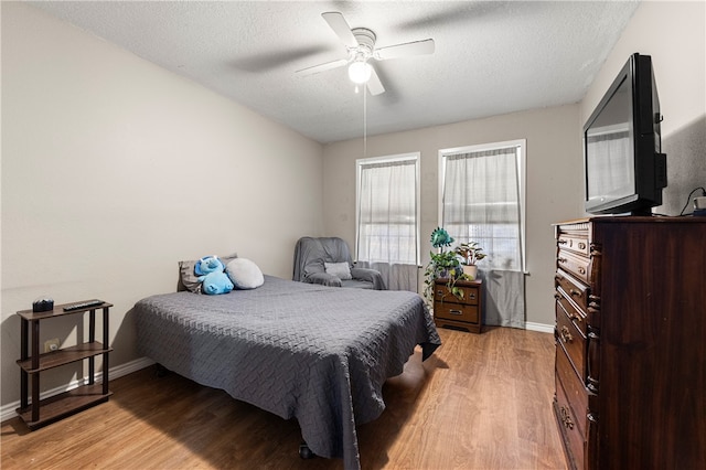 bedroom with ceiling fan, a textured ceiling, and light hardwood / wood-style flooring