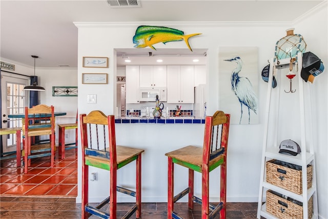 kitchen with tile counters, white cabinetry, crown molding, and decorative light fixtures