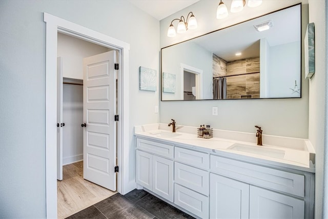 full bathroom with double vanity, a tile shower, a sink, and wood finished floors