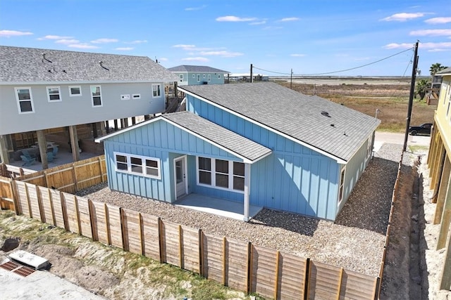 back of house with board and batten siding, roof with shingles, a fenced backyard, and a patio area
