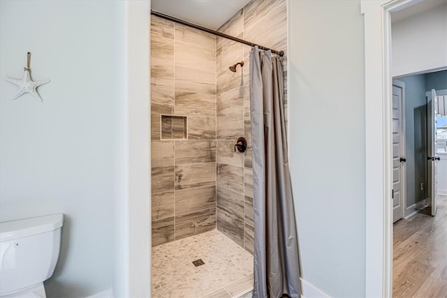 bathroom with tiled shower, wood finished floors, toilet, and baseboards