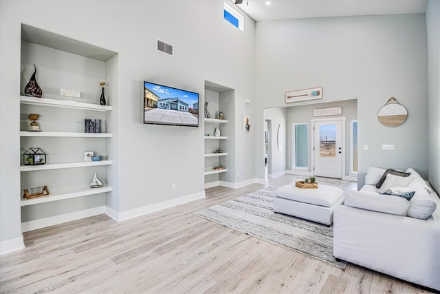 living area featuring baseboards, visible vents, wood finished floors, a high ceiling, and built in shelves