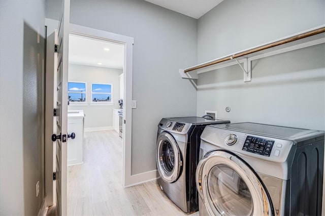 washroom with laundry area, baseboards, washer and clothes dryer, and light wood finished floors