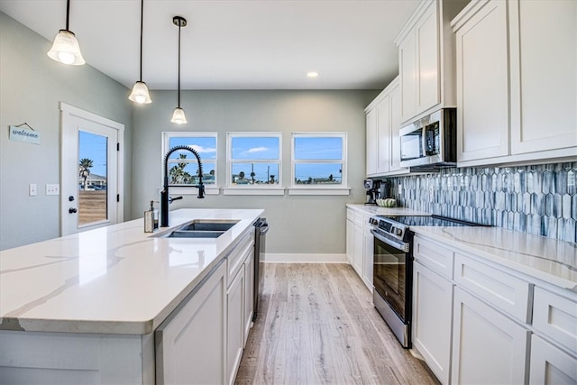 kitchen featuring light wood-style flooring, stainless steel appliances, a sink, baseboards, and backsplash