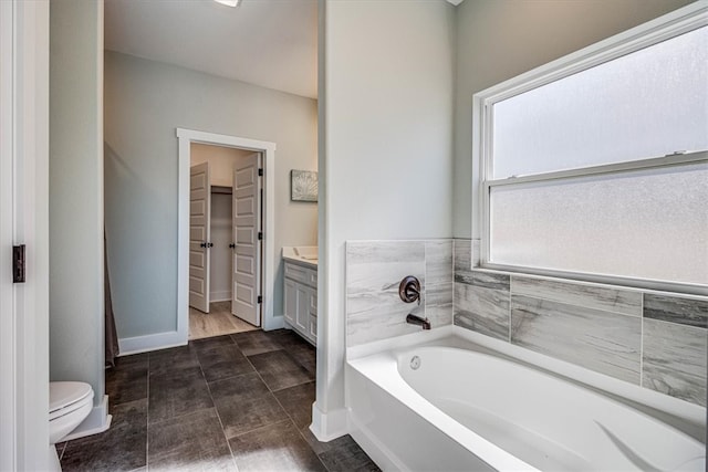 bathroom with a walk in closet, toilet, vanity, baseboards, and a bath