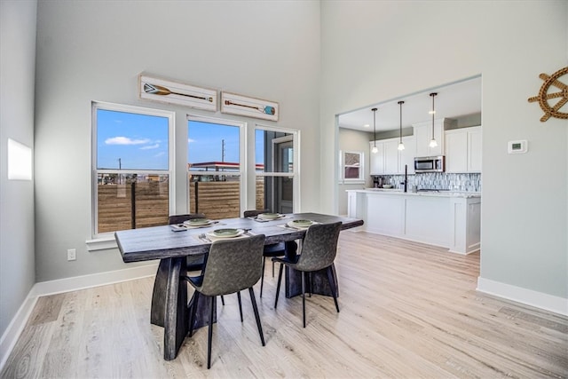 dining space with light wood-type flooring, a towering ceiling, and baseboards