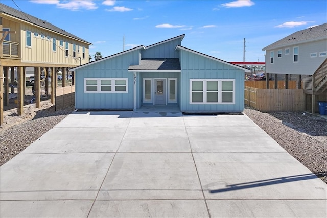 view of front of home featuring a patio area, fence, board and batten siding, and roof with shingles