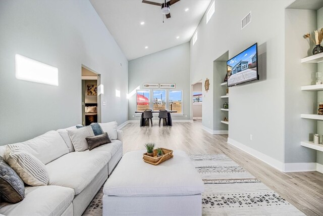 living room featuring light wood finished floors, visible vents, baseboards, a ceiling fan, and built in features