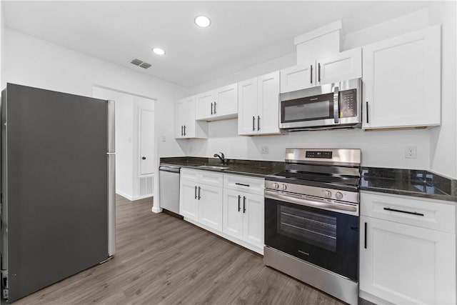 kitchen with dark wood-type flooring, white cabinetry, stainless steel appliances, dark stone counters, and sink