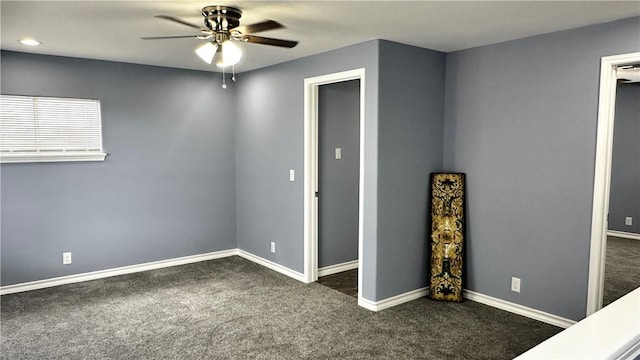 empty room featuring baseboards, dark carpet, and ceiling fan