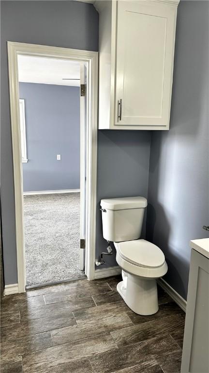 half bath featuring baseboards, vanity, toilet, and wood finished floors