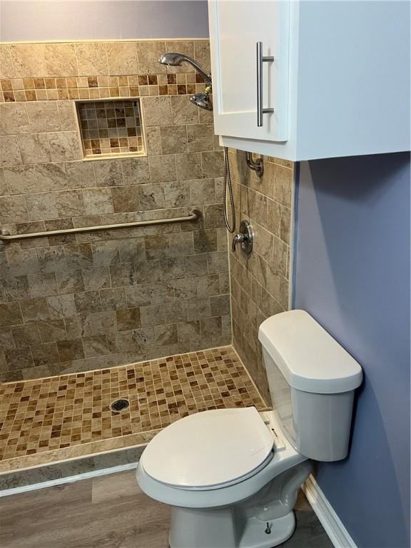 bathroom with a stall shower, baseboards, toilet, and wood finished floors