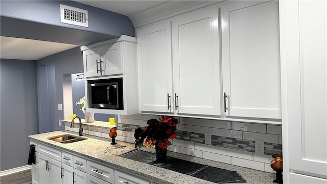 kitchen with visible vents, backsplash, white cabinets, a sink, and built in microwave