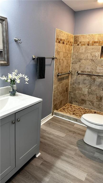 full bathroom featuring vanity, tiled shower, wood finished floors, and toilet