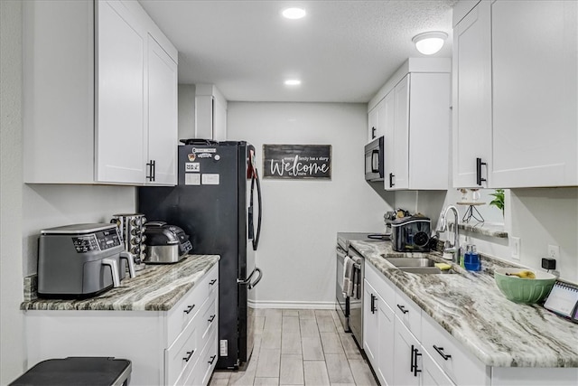 kitchen featuring black appliances, light stone counters, white cabinetry, light wood-type flooring, and sink