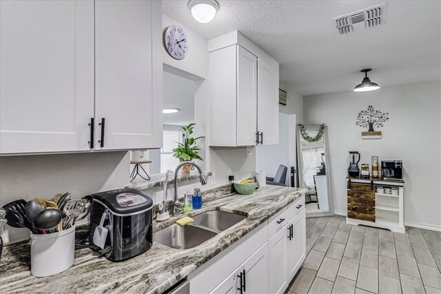 kitchen featuring white cabinetry, sink, a textured ceiling, and light stone counters