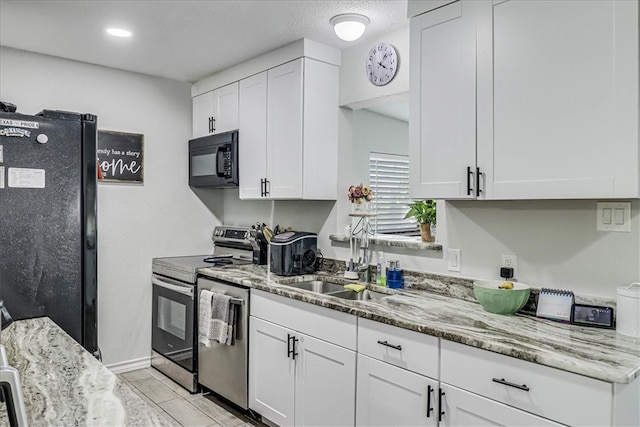 kitchen with black appliances, white cabinetry, sink, and light stone countertops