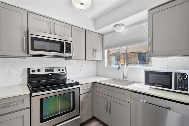 kitchen featuring stainless steel appliances, gray cabinets, tasteful backsplash, and sink