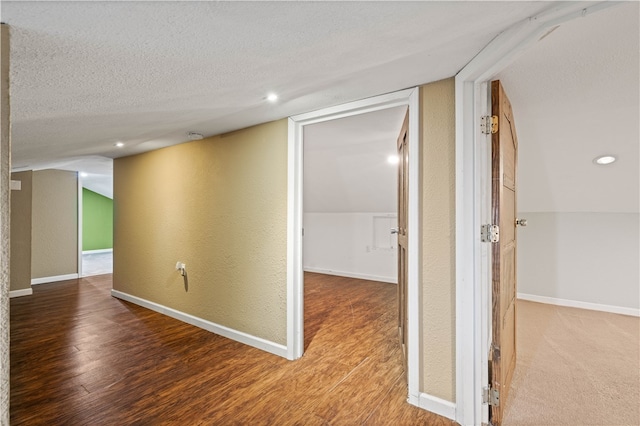 corridor featuring wood-type flooring, a textured ceiling, and vaulted ceiling