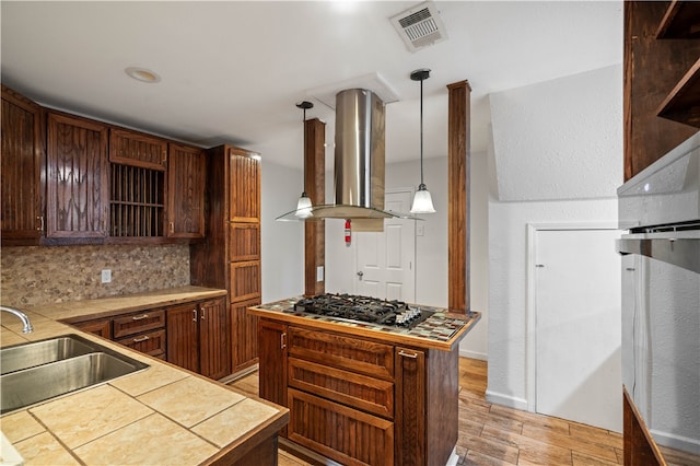 kitchen featuring island range hood, sink, decorative light fixtures, light hardwood / wood-style flooring, and stainless steel gas stovetop