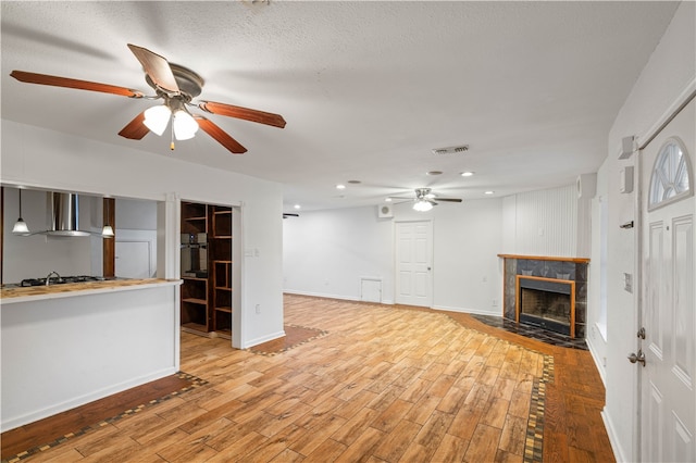 unfurnished living room with ceiling fan, a stone fireplace, light wood-type flooring, and a textured ceiling