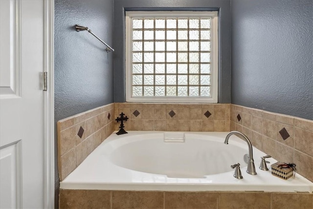 full bathroom featuring a wealth of natural light, a garden tub, and a textured wall