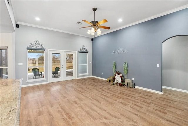 empty room featuring arched walkways, french doors, light wood finished floors, ornamental molding, and baseboards