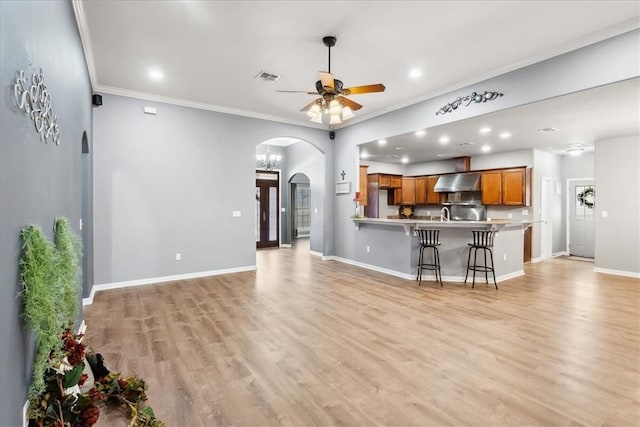 living area featuring arched walkways, light wood finished floors, a ceiling fan, ornamental molding, and baseboards