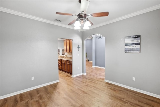 unfurnished dining area with arched walkways, light wood-style flooring, visible vents, baseboards, and crown molding